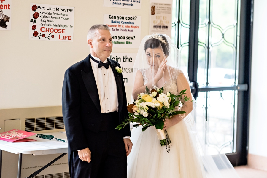 A bride whips away a tear right before walking down the isle with her father.